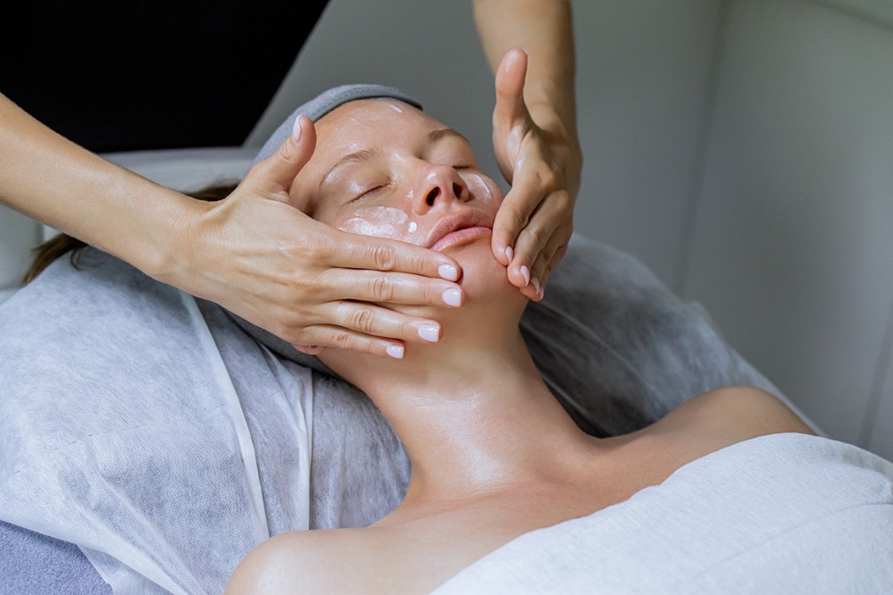 Woman receiving relaxing facial massage during skincare treatment - Medical Spa & Wellness By Michelle NP Close-up of a woman lying on a spa bed with eyes closed, receiving a soothing facial massage as part of a professional skincare treatment - Medical Spa & Wellness By Michelle NP